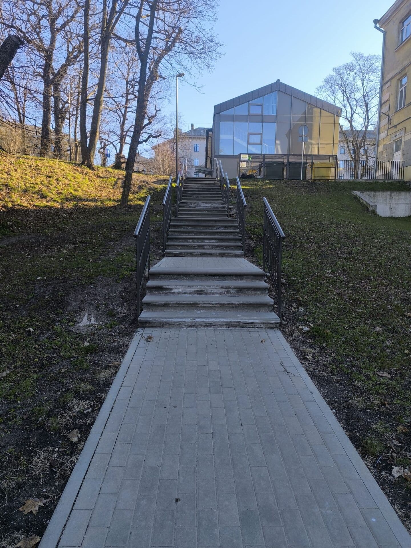 Garas āra kāpnes ar tumšām metāla margām zaļā nogāzē